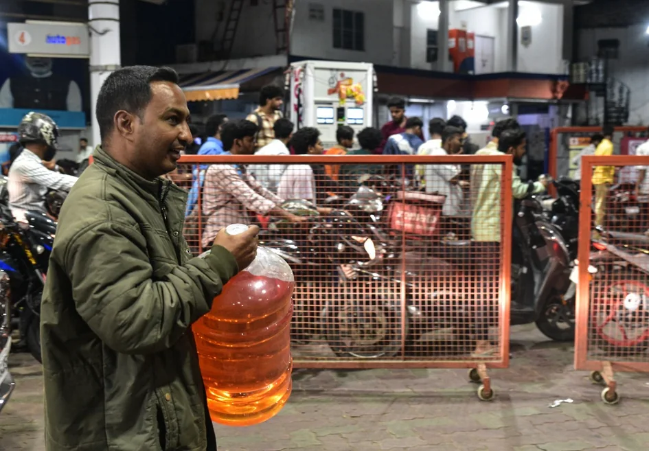 A motorcyclist carries petrol in a water container at a fuel station.