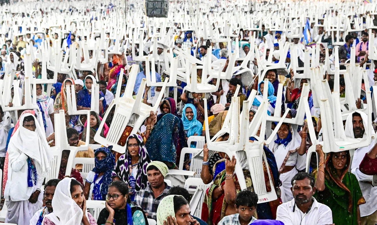 People shelter from rain with chairs during a public meeting at Parade Grounds in Telangana.
